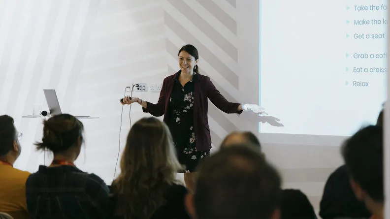 A woman smiling at a crowd as she does a presentation.