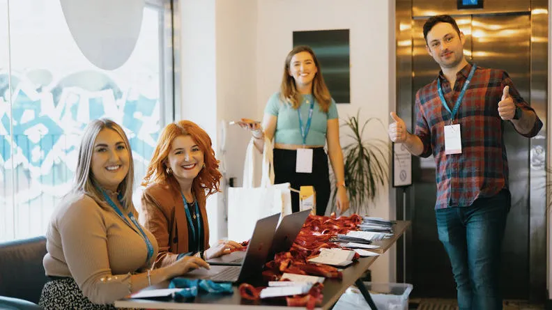 4 members of the Zengenti team smiling at the welcome registration desk at Velocity 2023.